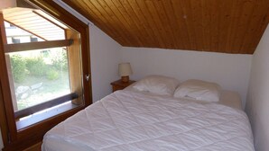 A bedroom with a wooden ceiling, a bed with white bedding, a nightstand with a lamp, and a window with a view of greenery. - 3-room apartment for 5 with balcony and parking at Les Contamines-Montjoie (Les Contamines-Montjoie)