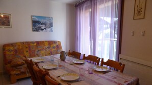 A dining area with a table set for four, surrounded by wooden chairs. A patterned sofa is against the wall, and a painting is hung above the table. - 3-room apartment for 5 with balcony and parking at Les Contamines-Montjoie (Les Contamines-Montjoie)