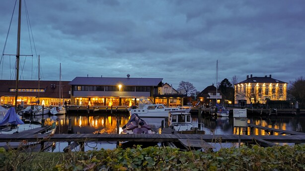 A marina with boats docked, a building with illuminated windows, and a large structure with lights on its facade. - Vacation with dog, and without dog (Varel)