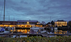 Ein Yachthafen mit vertäuten Booten, ein Gebäude mit beleuchteten Fenstern und eine große Struktur mit Beleuchtung an der Fassade.
