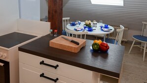 A kitchen with a wooden cutting board, a knife, and a bowl of vegetables on the counter. There is a dining table with chairs in the background. - Vacation with dog, and without dog (Varel)