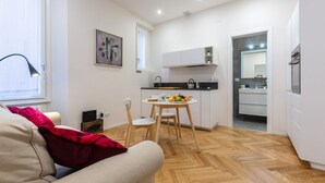 Un espacio habitable compacto con kitchenette, comedor y sofá con una manta roja.