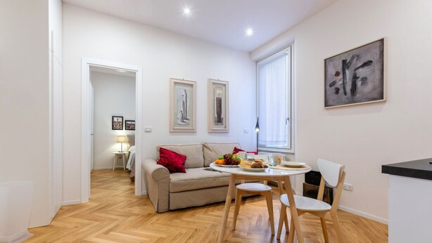 Una sala de estar moderna con sofá, mesa de comedor, sillas, una zona de cocina y obras de arte en las paredes.