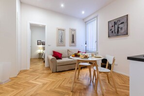 Una sala de estar moderna con sofá, mesa de comedor, sillas, una zona de cocina y obras de arte en las paredes.