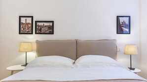 Una cama con dos almohadas, cabecera, dos mesitas de noche con lámparas y dos cuadros enmarcados en la pared.