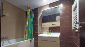 Un baño con una bañera, un lavabo con un espejo encima y un perchero con una toalla de colores.