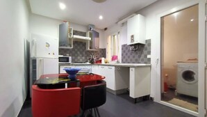 Una cocina compacta con comedor, armarios blancos, horno empotrado y lavadora en la habitación contigua.