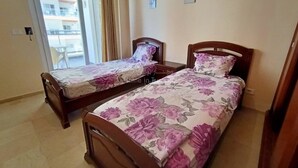 Dos camas de madera con ropa de cama floral en una habitación con puerta corrediza de vidrio al exterior.