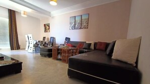Una sala de estar moderna con un sofá negro, una mesa de centro y un mueble para televisión. Hay tres cuadros enmarcados en la pared y una ventana con cortinas.