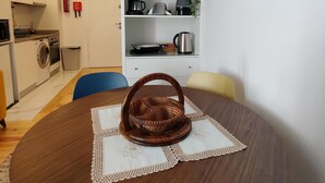 A dining area with a round wooden table, a woven basket, and a white lace table runner. - Cais de Gaia Historic Loft (Vila Nova de Gaia)