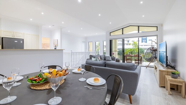 A modern apartment with a dining area, a grey sofa, and a balcony with a TV. - Resthaven, 3b Messines Street (Shoal Bay)