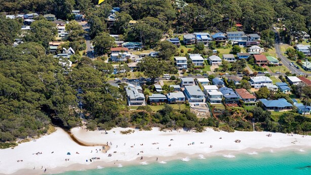 Luchtbeeld van een kustgebied met woningen, een strand en helder turquoise water.