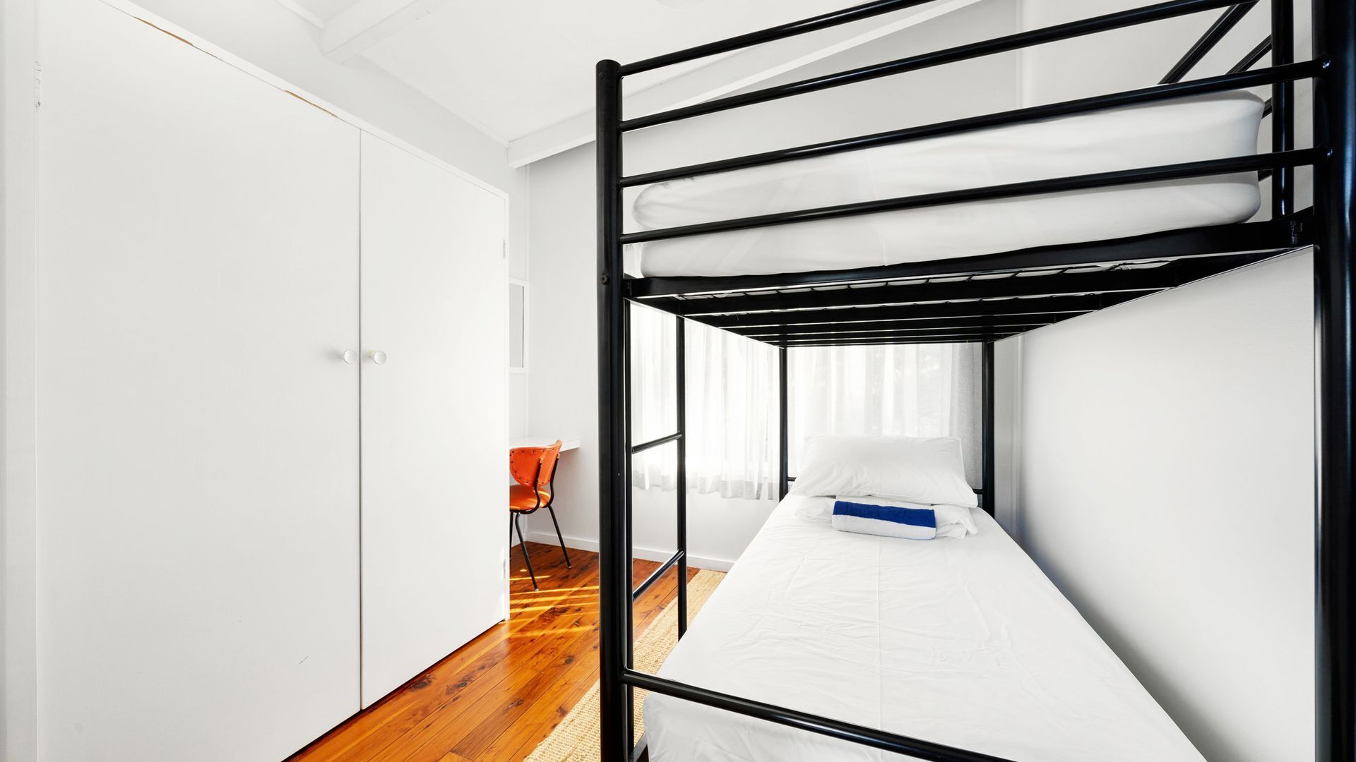 A bunk bed room with a wooden floor, white walls, and a small orange chair.