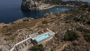 An aerial view of a coastal property with a swimming pool, lounge chairs, and a rocky landscape. - Pristine Seaview Villa , with 5-Star Resort Access (Faliraki)