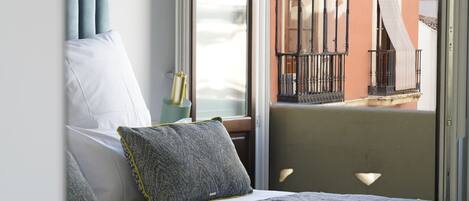 A bedroom with a bed, pillows, and a view of a balcony with a railing.