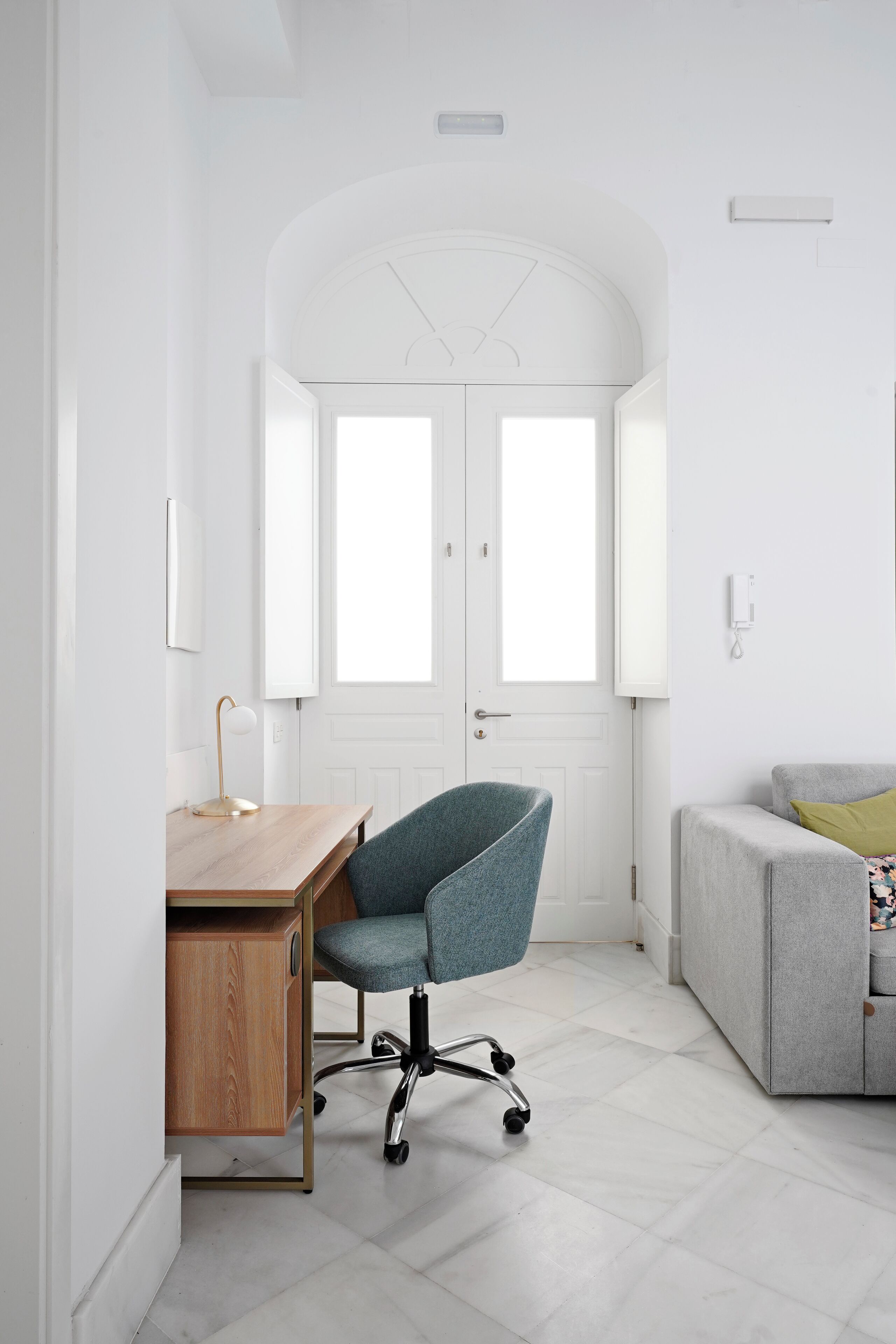 Un espace de bureau moderne avec un bureau en bois, une chaise de bureau bleue, un canapé gris et une porte blanche dotée de fenêtres.