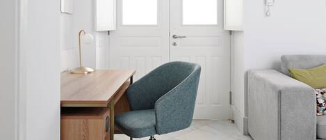 Un espace de bureau moderne avec un bureau en bois, une chaise de bureau bleue, un canapé gris et une porte blanche dotée de fenêtres.