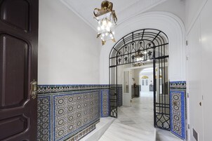 Um corredor com porta de madeira escura, paredes brancas e azulejos estampados em azul.