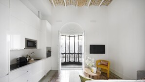 A modern kitchen with white cabinets, a microwave, and a sink. There is a balcony with a black railing and a view of buildings. - Numa Seville Solea (Seville)