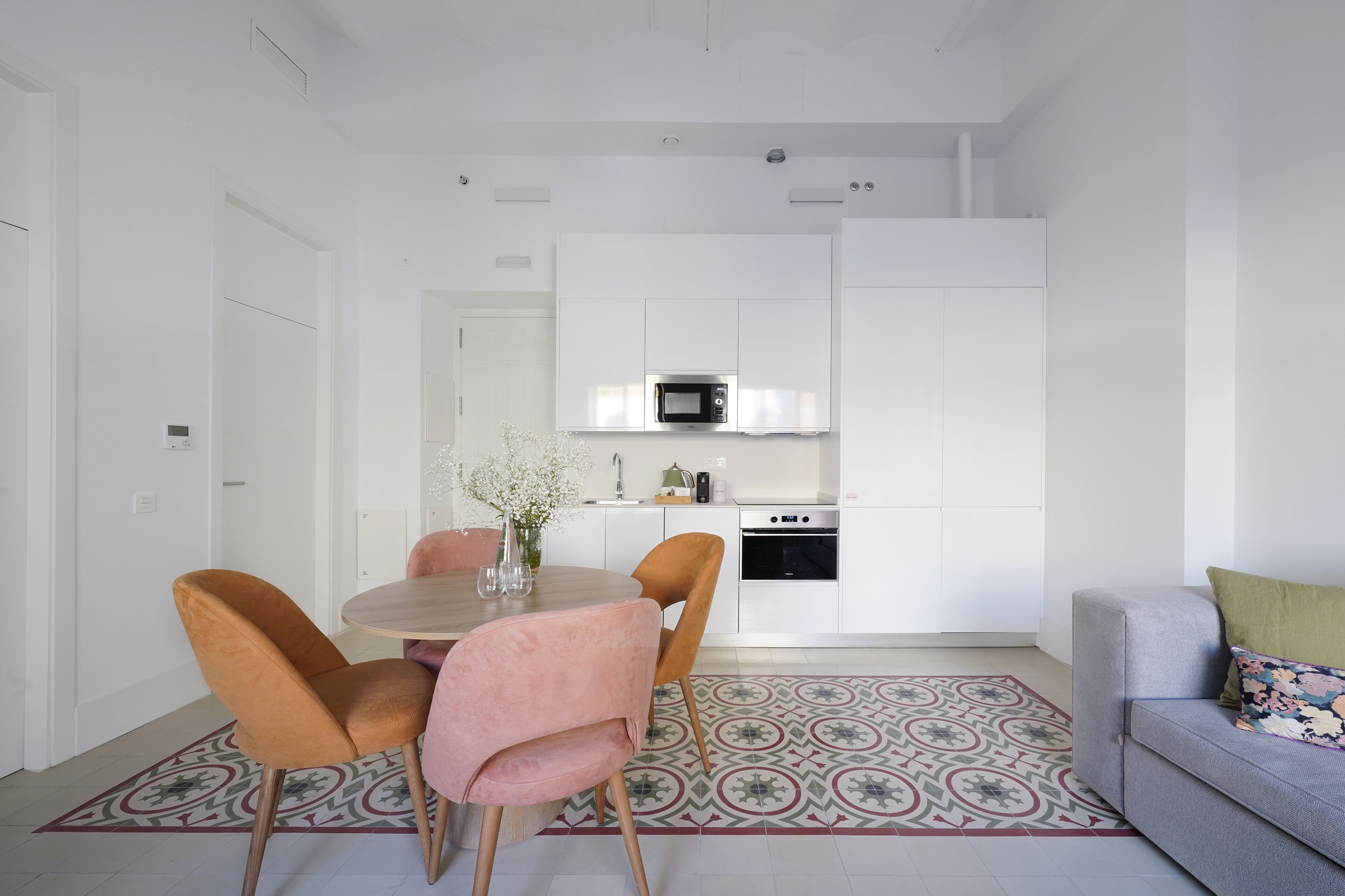 A modern kitchen with white cabinets, a microwave, and an oven. There is a dining area with a round table and chairs.