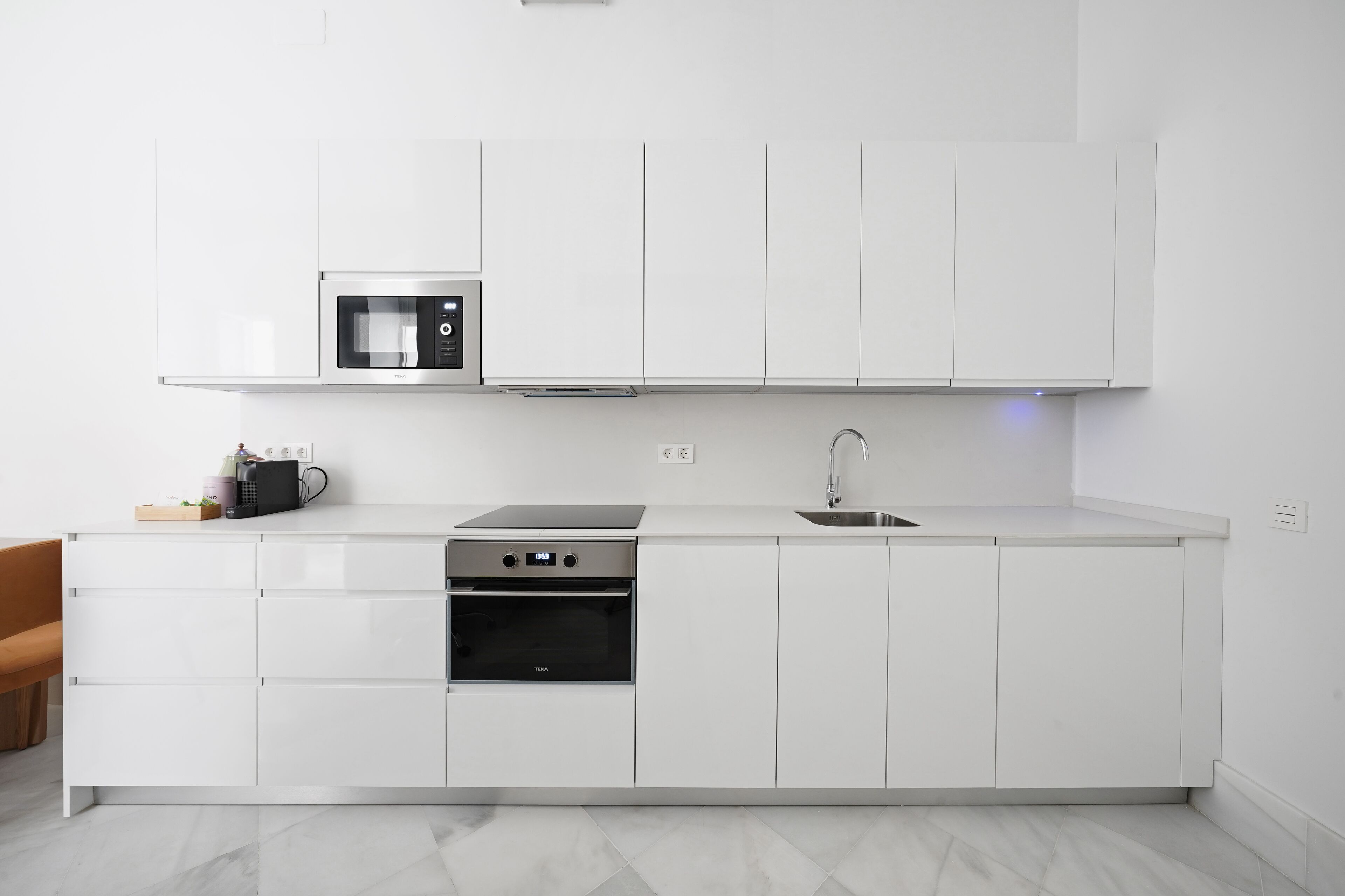 A modern kitchen with white cabinets, a built-in microwave, a stove, and a sink.