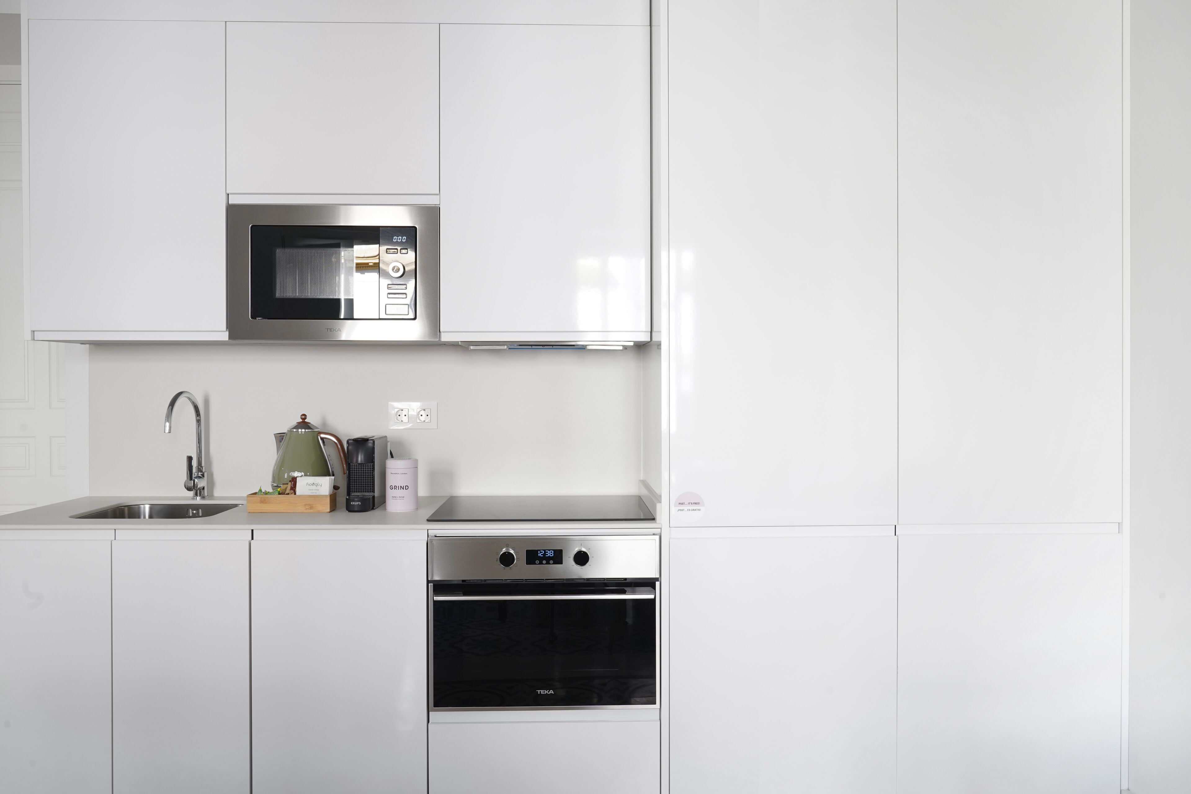 Una cocina moderna con armarios blancos, microondas de acero inoxidable, cafetera y horno empotrado.