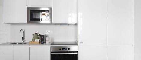Una cocina moderna con armarios blancos, microondas de acero inoxidable, cafetera y horno empotrado.