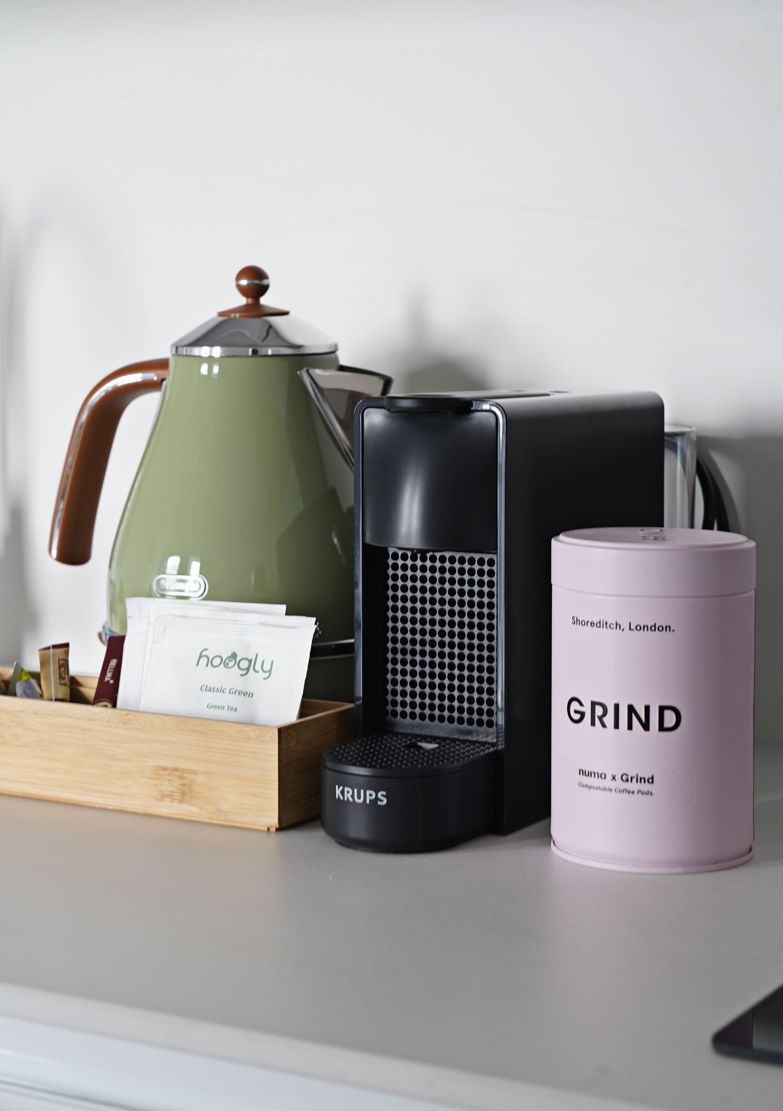 Une machine à café, une bouilloire, un récipient pour les capsules de café et une tasse à café sont posés sur une table.