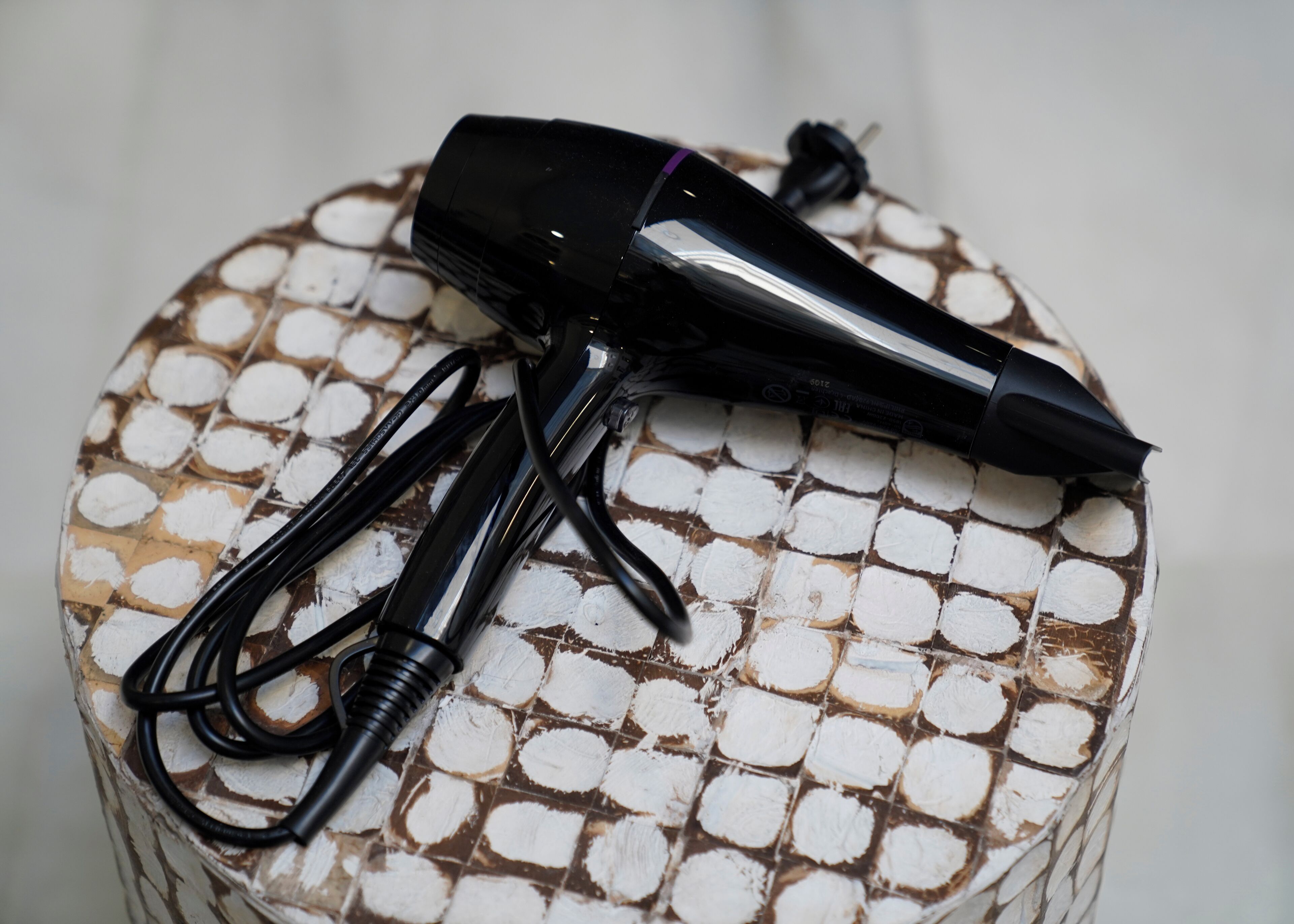 A round, textured table with a black hairdryer and its cord on it.