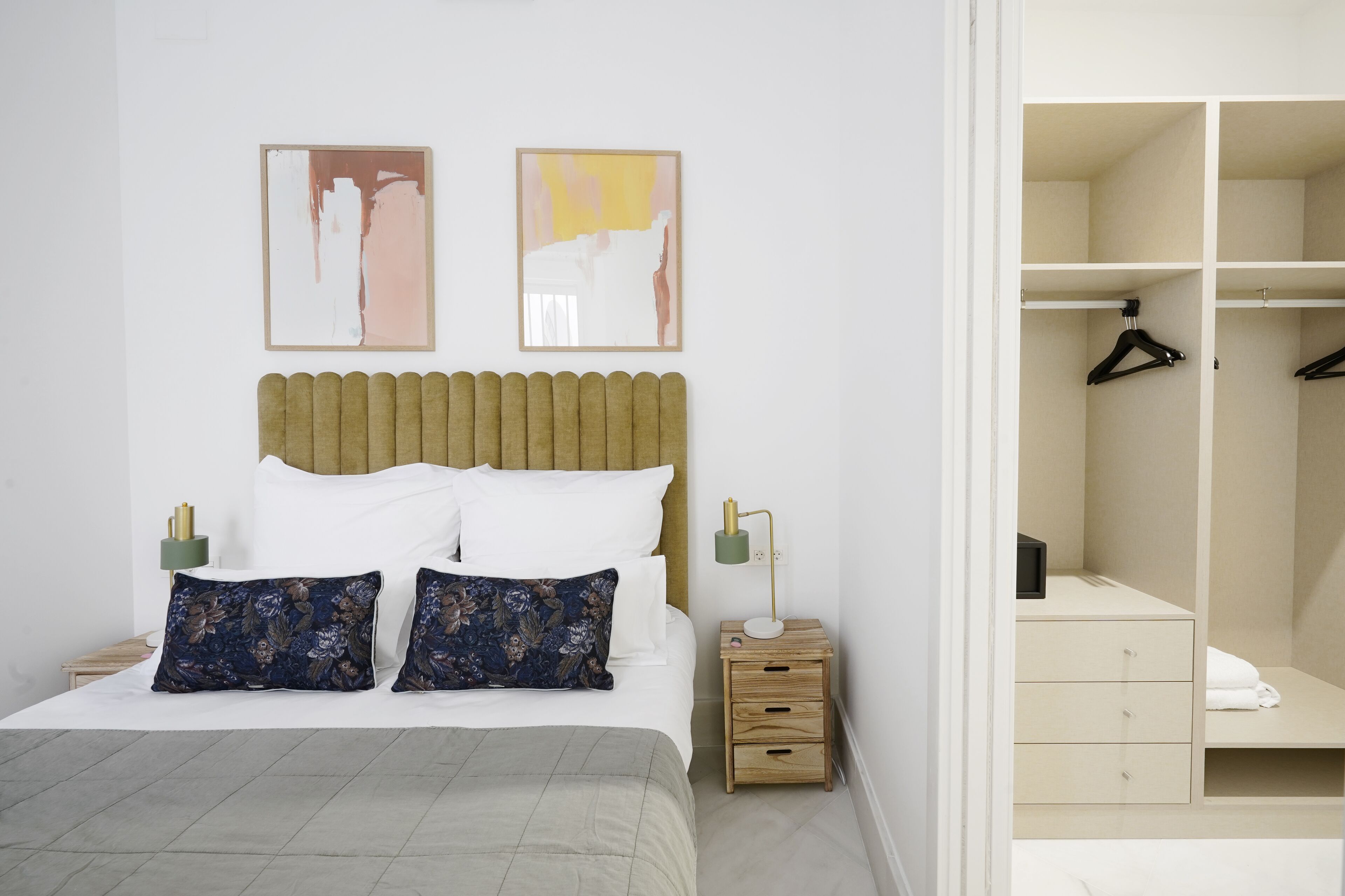 Une chambre à coucher bien rangée, avec un lit, des tables de chevet, une commode, une armoire et deux tableaux abstraits accrochés au mur.