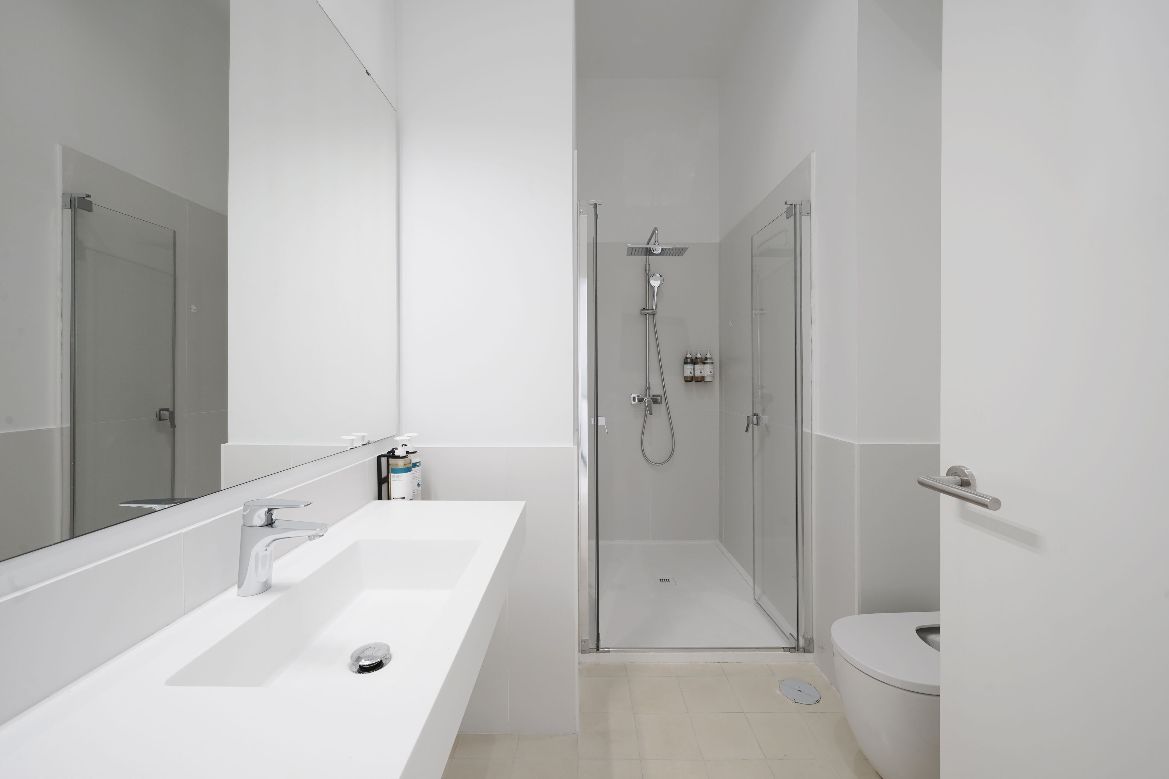 Egy modern fürőszoba, melyben fehér mosdókagyló, tükör, zuhanyzó és WC található.