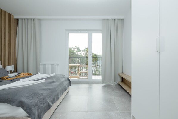 A modern bedroom with a large bed, a balcony, and a view of the outdoors.
