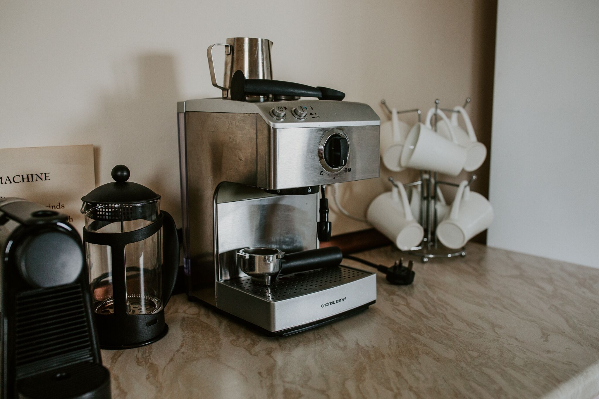 A coffee machine with a drip tray, a glass carafe, and a coffee press on a marble countertop.