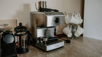 A coffee machine with a drip tray, a glass carafe, and a coffee press on a marble countertop.