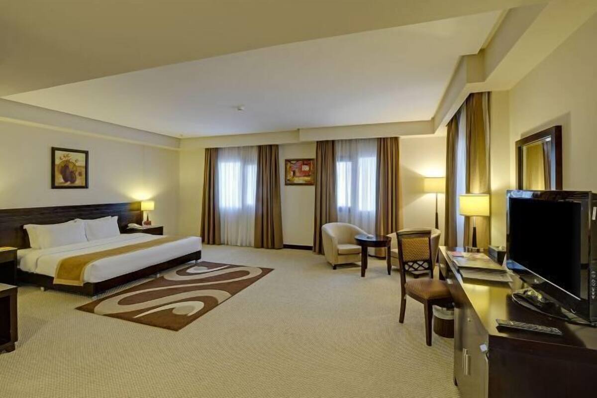 A hotel room with a bed, a desk with a TV, a chair, and a lamp.