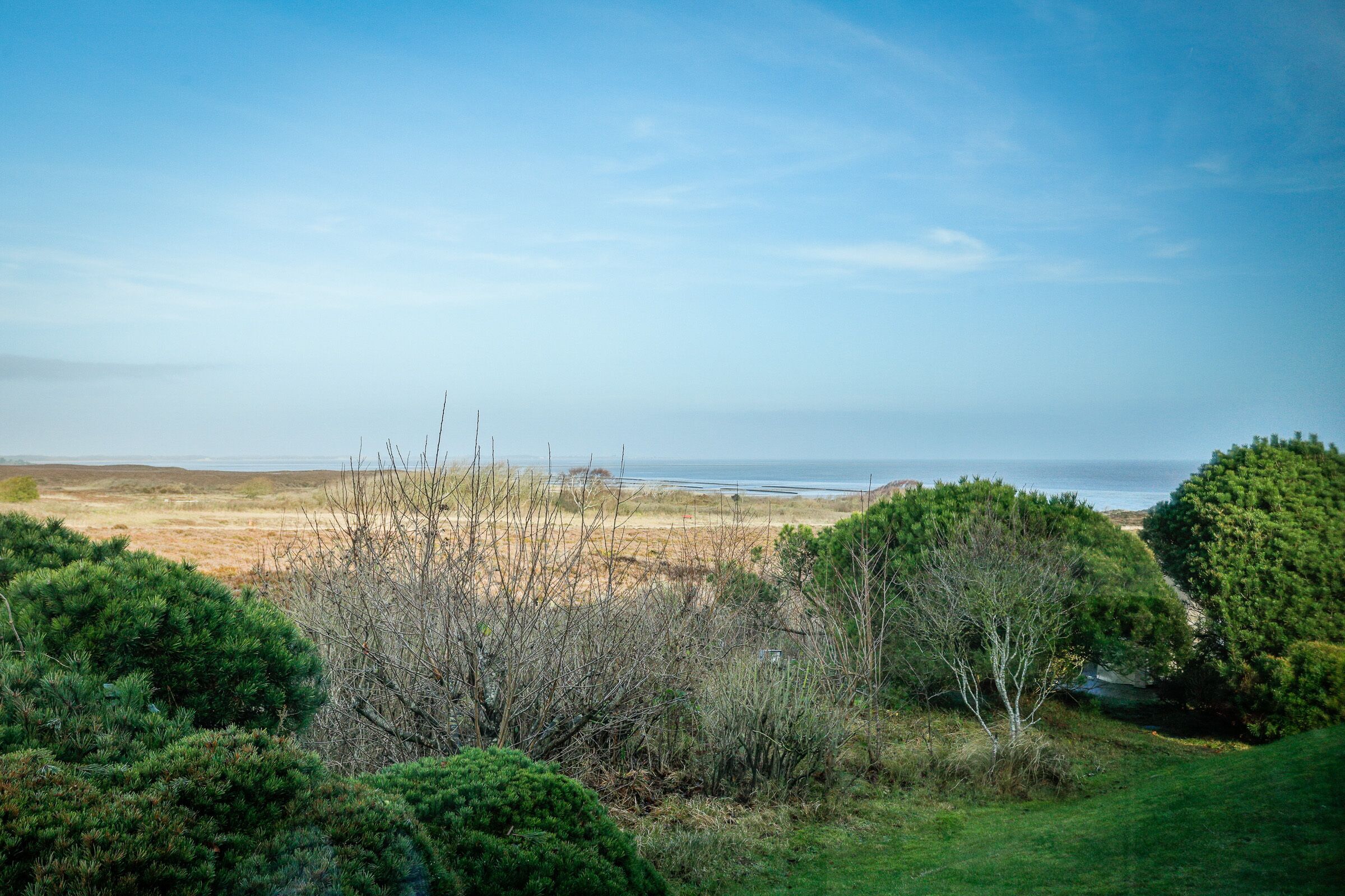 Paisagem costeira com vista para o mar, rodeada por vegetação verde e céu claro.