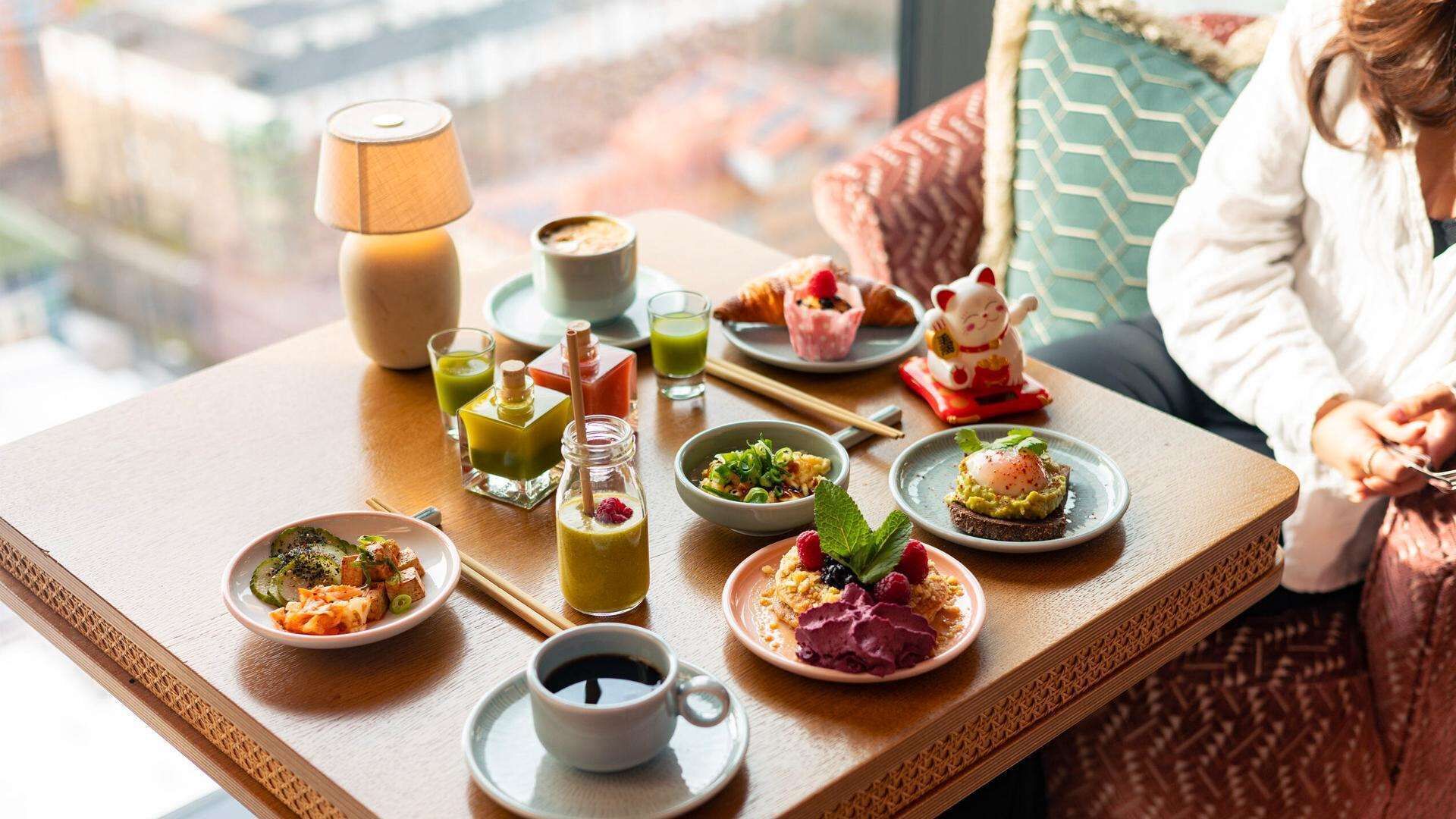 Una mesa de comedor con diversos platos y bebidas, una lámpara y vista a la ciudad.