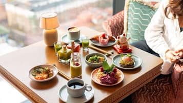 Una mesa de comedor con diversos platos y bebidas, una lámpara y vista a la ciudad.
