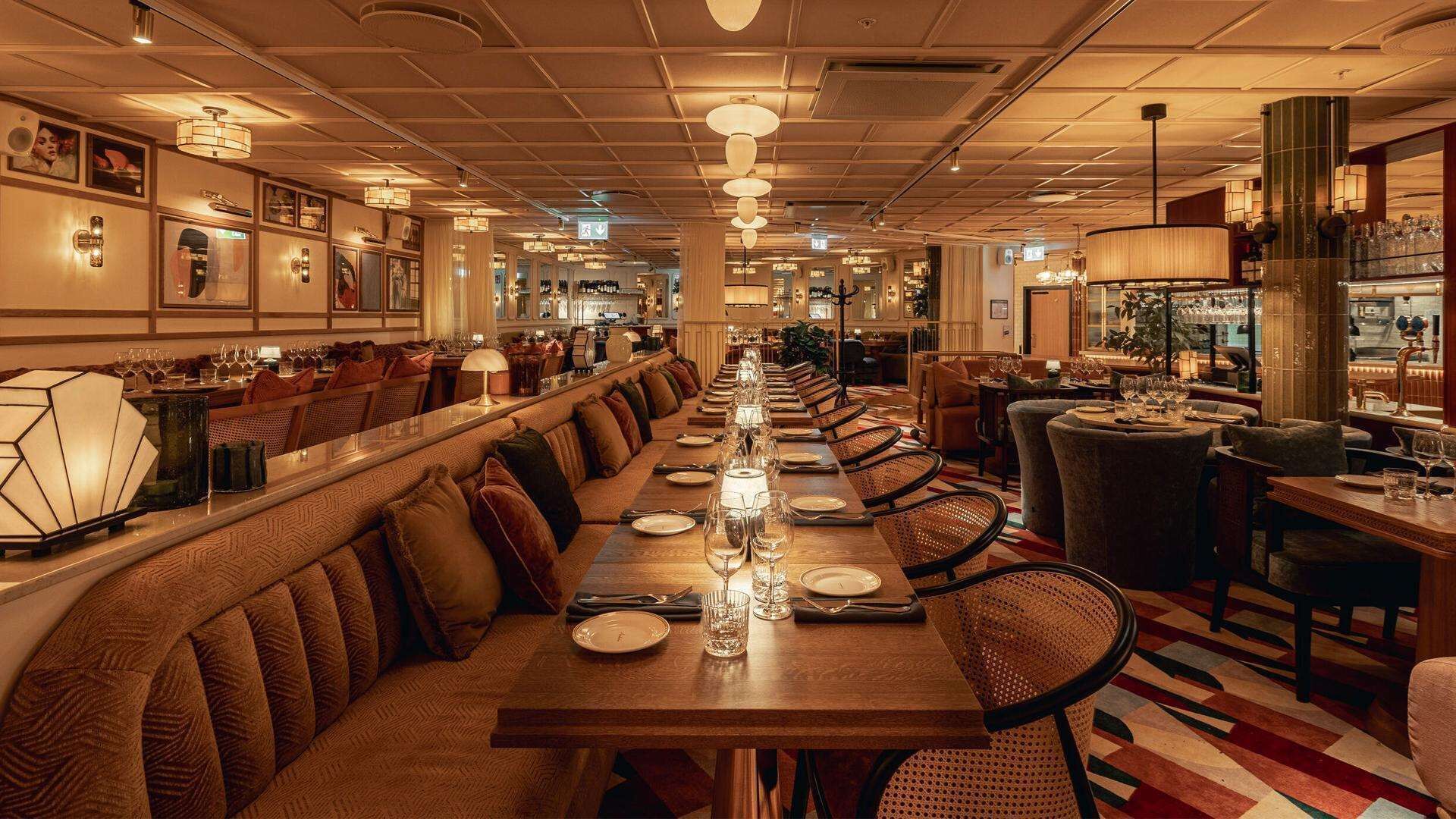Una larga mesa de comedor con múltiples sillas, una zona de bar y un área de estar con bancos acolchados.