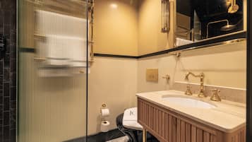 Un baño con cabina de ducha de vidrio, un lavamanos blanco con detalles dorados y un inodoro con una toalla sobre el asiento.