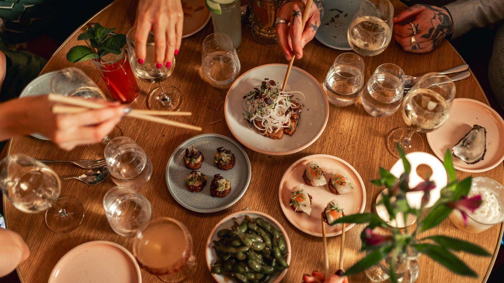 A round wooden table with various dishes, drinks, and utensils, suggesting a dining setting.