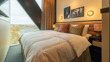 A hotel room with a large bed, a nightstand, a lamp, and a view of the outdoors.