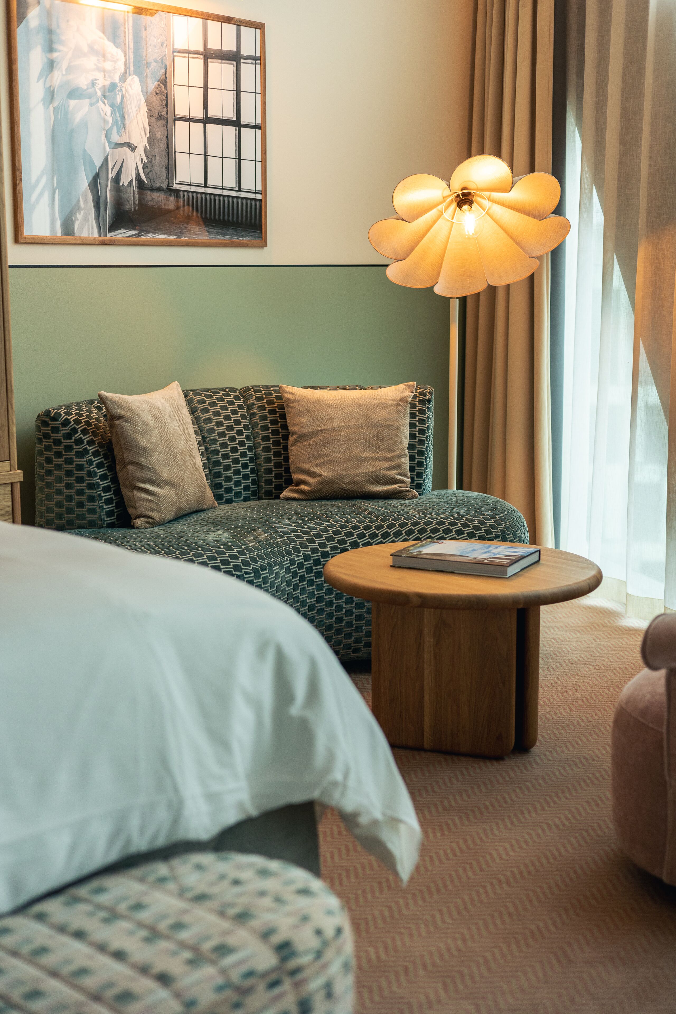 Ein Hotelzimmer mit einem großen Bett, einer Sitzecke, einem runden Holztisch und einer Wandleuchte.