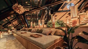 A cozy, modern interior with a large, cushioned seating area, wooden beams, and a variety of plants. - Jacy'z Hotel & Resort (Gothenburg)