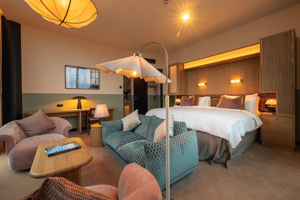 A modern hotel room with a large bed, a sofa, a small table, and a desk.