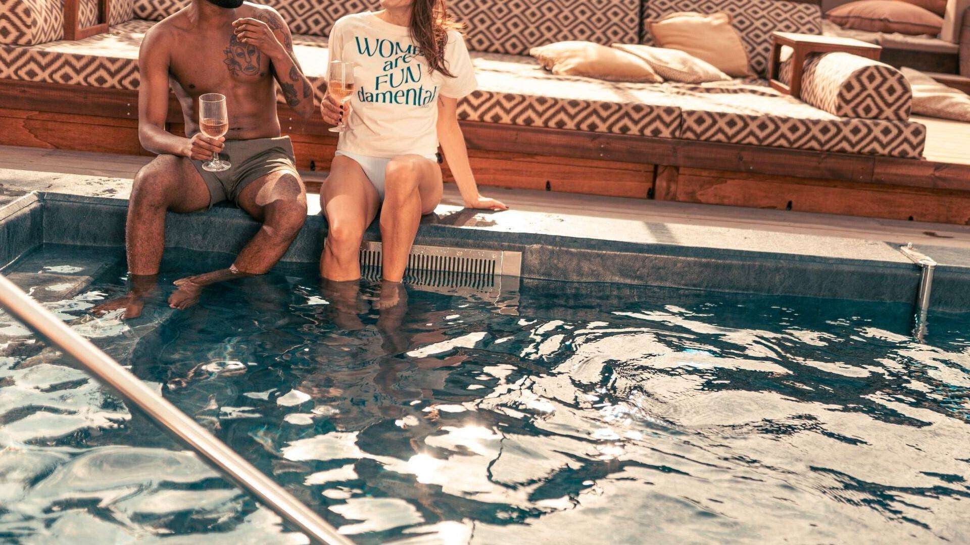 Dues persones assegudes a la piscina, amb un sofà estampat al fons.