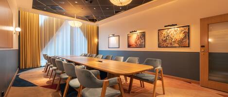 A conference room with a long table, multiple chairs, and a large painting on the wall.