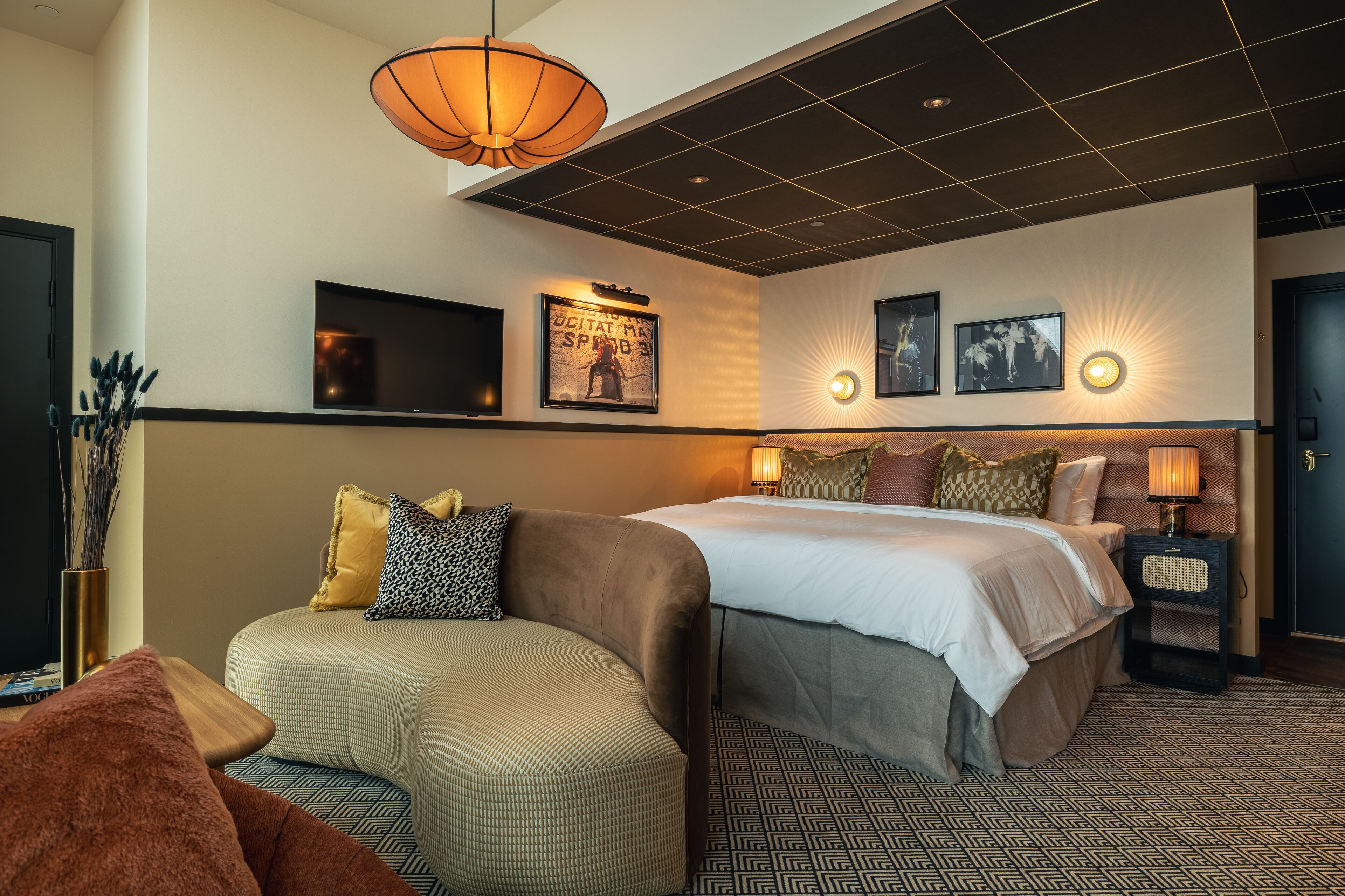 Une chambre d’hôtel équipée d’un lit, d’un canapé, d’une télévision et de lampes fixées au mur.