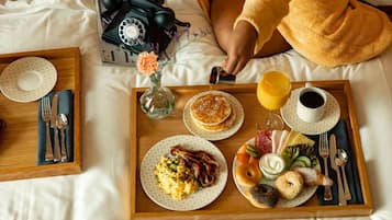 A breakfast tray with pancakes, eggs, bacon, bagels, and juice on a bed.