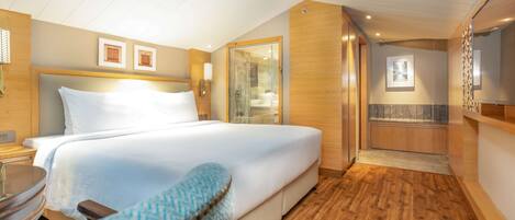 A hotel room with a large bed, a wooden floor, a glass shower enclosure, and a small seating area.